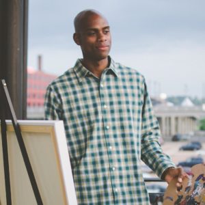 Portrait of Omari Booker standing in front of his easel, overlooking the city.